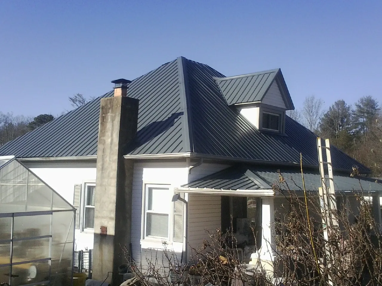 Dark blue standing seam metal roof on a white farmhouse with dormer — Slate & Tile Roof Repair by Roofing Brothers in Haven