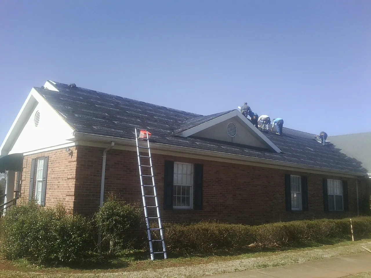 Crew tearing shingles off a brick ranch roof with a ladder set — Emergency Roof Repair work by our crew in Haven