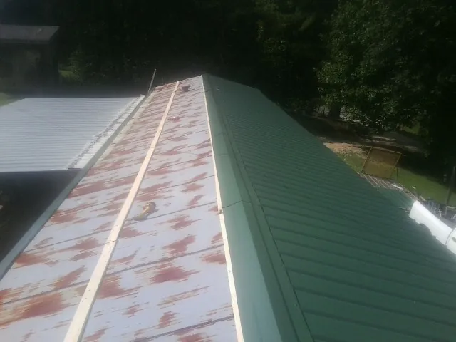 Old rusted panels beside newly installed green metal roofing — Wind Damage Roof Repair by Roofing Brothers in Haven