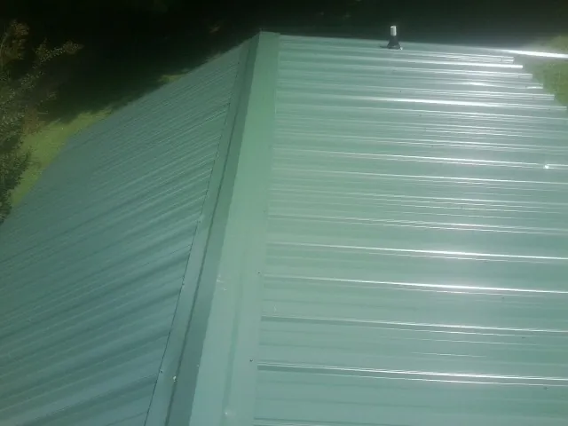 New green metal panels meeting at the ridge of a roof — Flat Roof Repair work by our crew in Haven