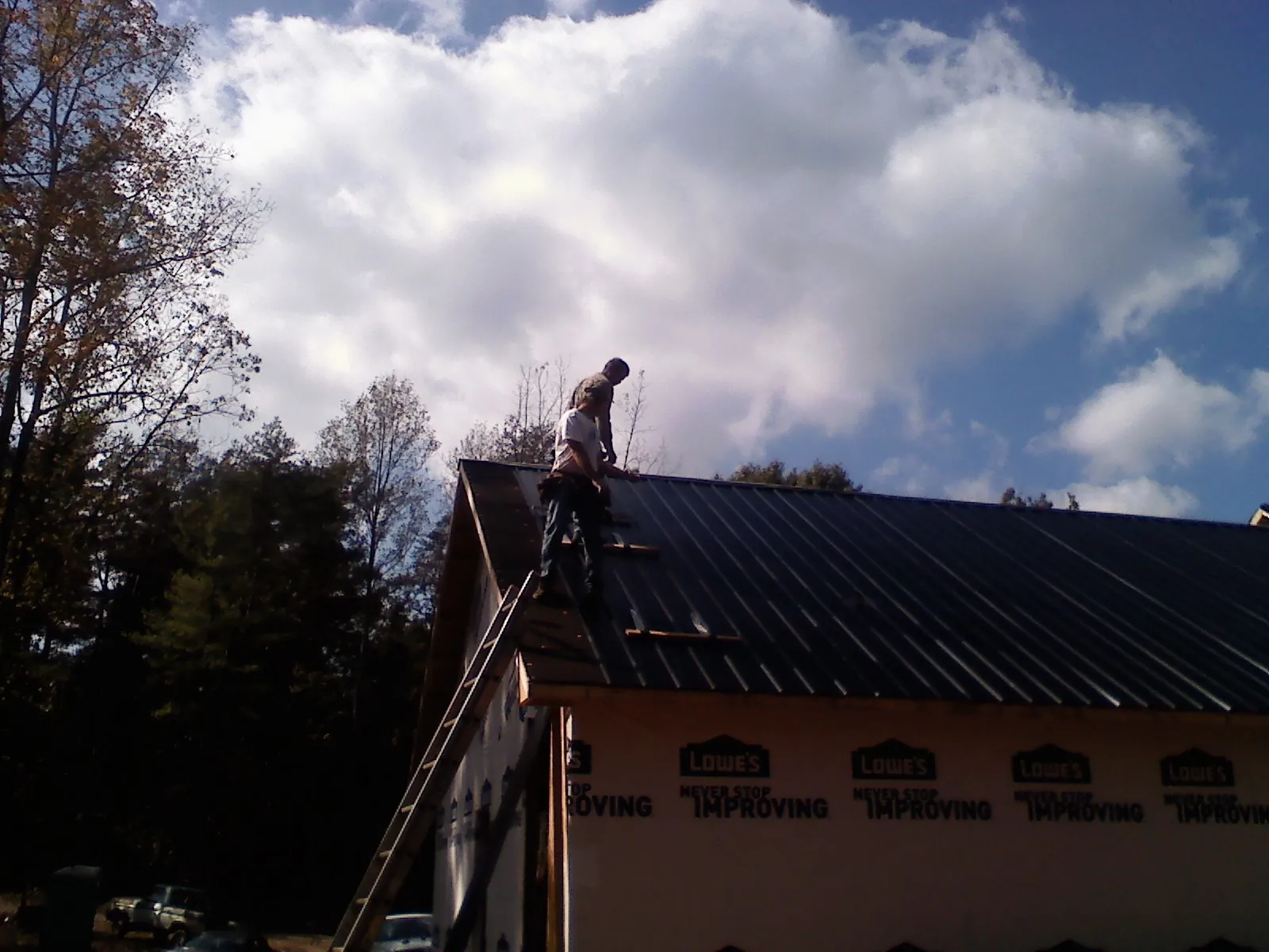 Roofer fastening dark metal panels high against a cloudy sky, from a Roof Inspection job in Haven